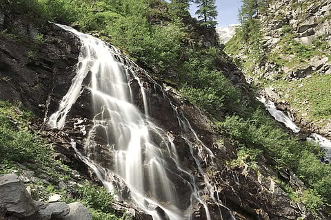 Wasserfall im Schödertal nahe dem Hotel Tauernhof Großarl, umgeben von grünen Bäumen und einer felsigen alpinen Landschaft.