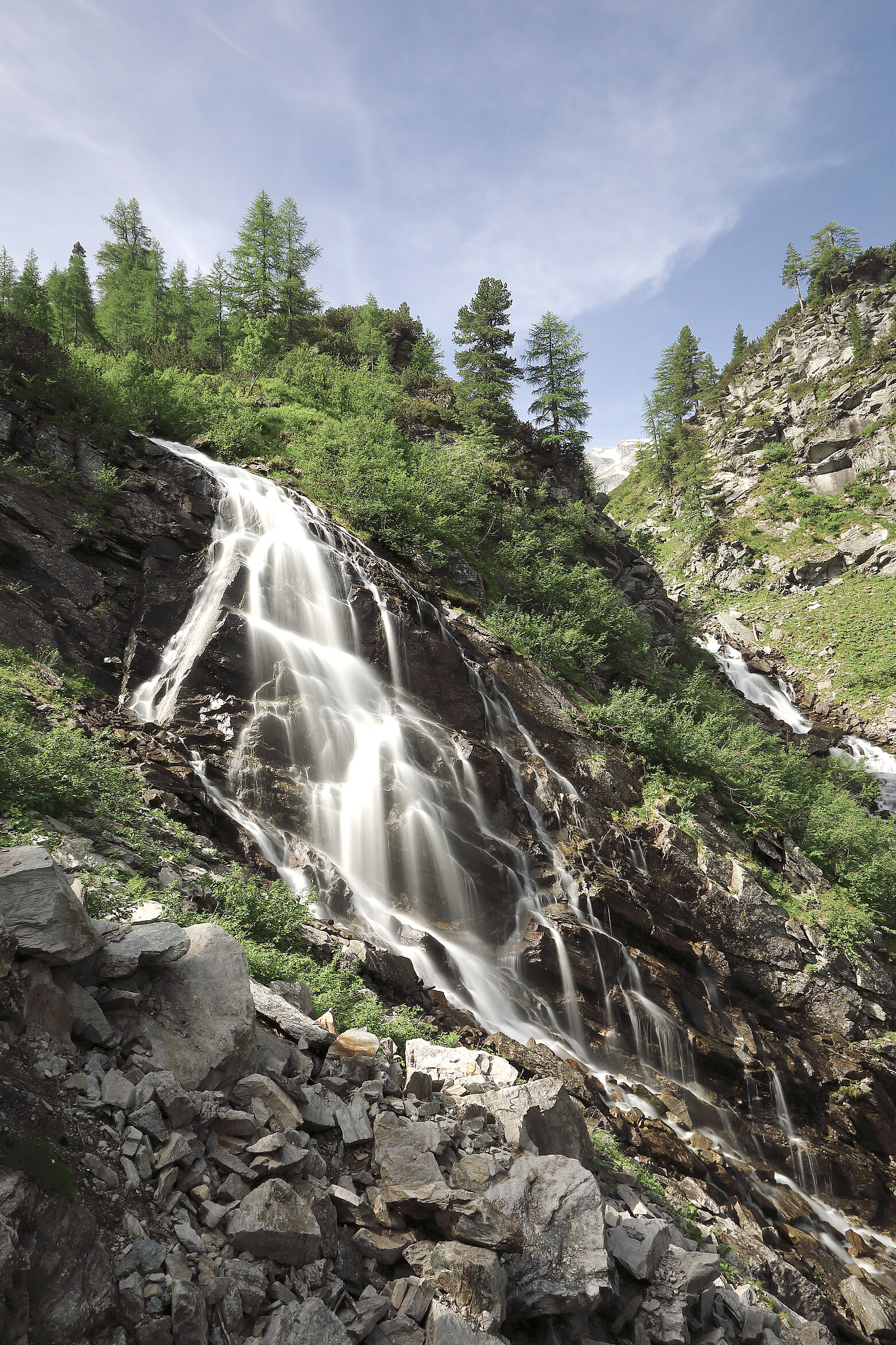 Wasserfall im Schödertal nahe dem Hotel Tauernhof Großarl, umgeben von grünen Bäumen und einer felsigen alpinen Landschaft.