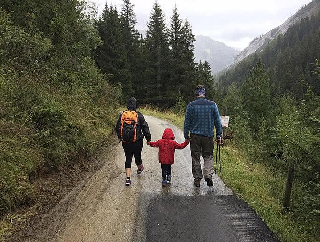 Familie mit Kind beim Wandern auf einem Forstweg, umgeben von Wäldern und Bergen