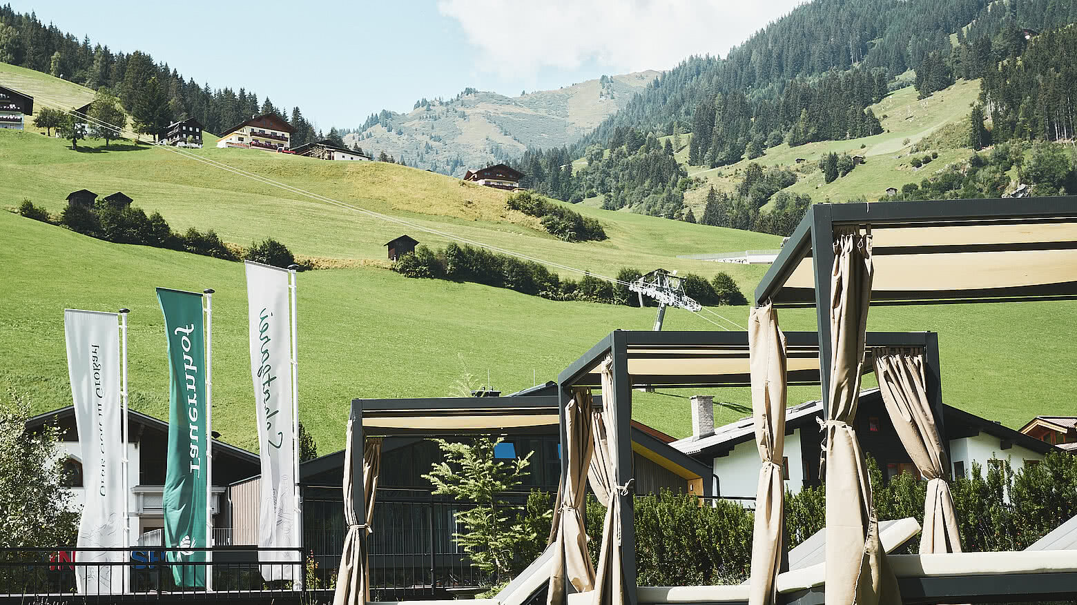 Sonnenterrasse des Hotels Tauernhof Großarl mit Blick auf grüne Wiesen, umliegende Chalets und die Berglandschaft der Alpen.
