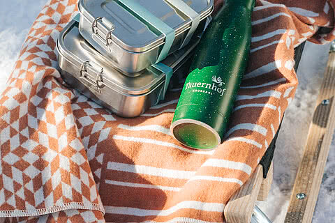 Picknick-Set mit Edelstahlboxen, Thermosflasche vom Tauernhof und gemütlicher Decke auf einem Schlitten im Schnee