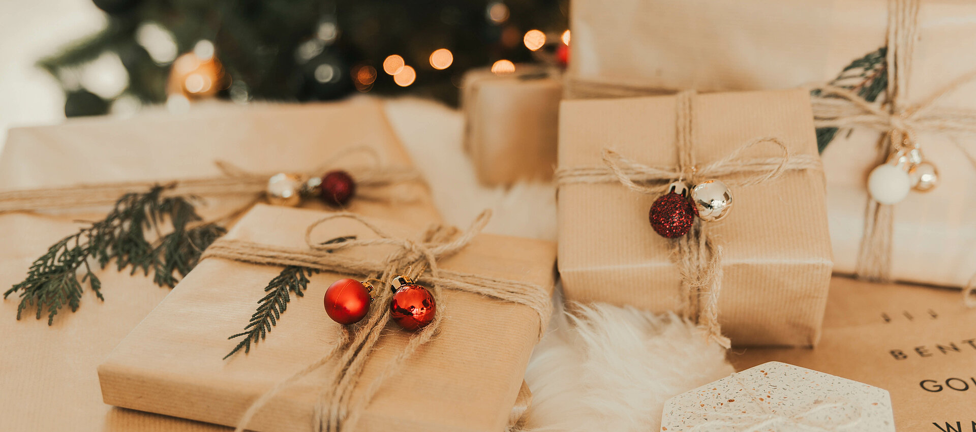 Weihnachtlich verpackte Geschenke mit natürlicher Dekoration aus Tannenzweigen und Kugeln vor einem geschmückten Weihnachtsbaum im Tauernhof in Großarl
