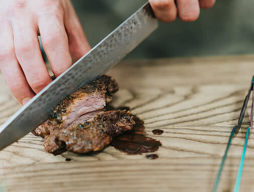 Eine Hand schneidet ein Stück saftiges Fleisch mit einem großen Messer auf einem Holzbrett im Tauernhof Großarl