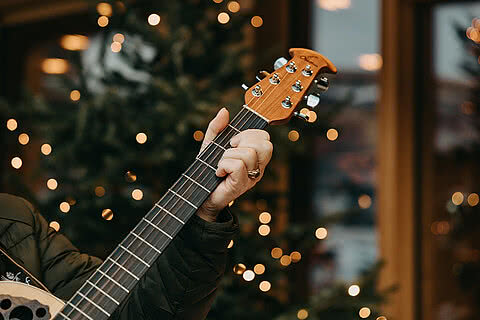 Nahaufnahme einer Gitarre vor einem weihnachtlich geschmückten Hintergrund mit Lichterketten im Tauernhof Großarl.
