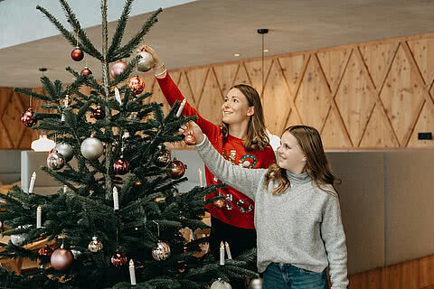 Mutter und Tochter schmücken einen Weihnachtsbaum mit Kugeln und Kerzen im Tauernhof Großarl.“