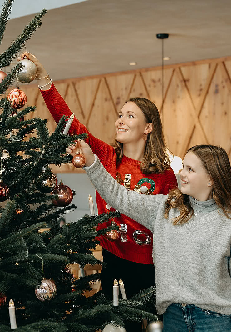 Mutter und Tochter schmücken einen Weihnachtsbaum mit Kugeln und Kerzen im Tauernhof Großarl.“
