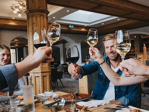 Fünf Freunde stoßen mit Weingläsern an. Sie sitzen in Die Schatzerei, dem Restaurant im Tauernhof. Das Ambiente ist modern, aber gemütlich.