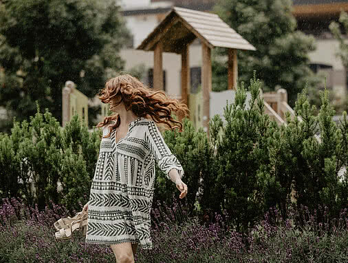 Familienhotel Österreich mit Pool, Tauernhof in Großarl: Eine Frau mit roten, langen Haaren und einem weitern Kleid läuft durch den Garten des Tauernhofes.