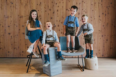 Die Kinder der Gastgeberfamilie des Hotel Tauernhof in Großarl lachen fröhlich in traditioneller Tracht vor einer Holzwand.