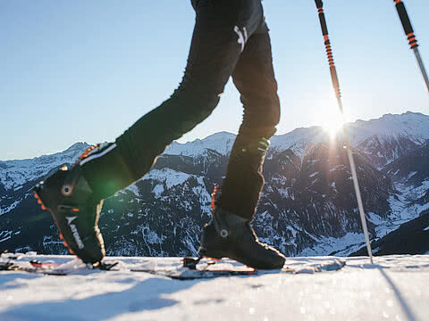 Nahaufnahme eines Skitourengehers in den Alpen bei Sonnenschein mit Blick auf verschneite Berggipfel