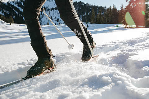 Nahaufnahme der Beine eines Skitourengehers, der durch frischen Schnee in einer verschneiten Berglandschaft stapft