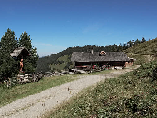 Die Maurachalm, eine traditionelle Berghütte aus dunklem Holz mit Schindeldach, umgeben von blühenden Geranien.