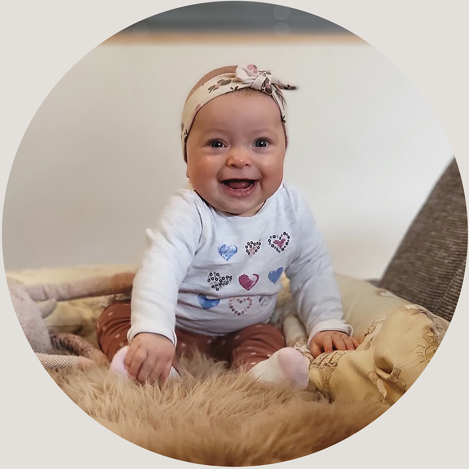 Glückliches Baby Magdalena mit Stirnband, sitzt lächelnd auf einer weichen Decke im Hotel Tauernhof Großarl.