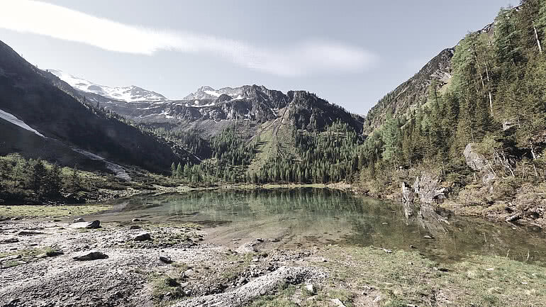 Ein idyllischer Bergsee mit klarem Wasser, umgeben von Wäldern und beeindruckenden Gipfeln erreichbar vom Hotel Tauernhof in Großarl.