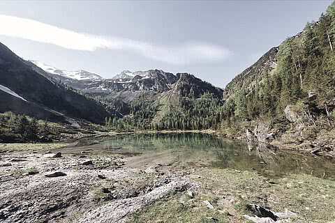 Ein idyllischer Bergsee mit klarem Wasser, umgeben von Wäldern und beeindruckenden Gipfeln erreichbar vom Hotel Tauernhof in Großarl.