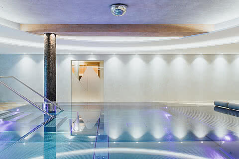 Eleganter Indoor-Pool im Hotel Tauernhof Großarl mit stimmungsvoller Beleuchtung, modernen Design-Elementen und entspannter Atmosphäre.