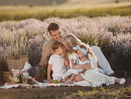 Big family on a picnic in a lavender field Eine Familie, bestehend aus Vater, Mutter und zwei Kindern, machen vor einem Lavendelfeld ein Picknick.