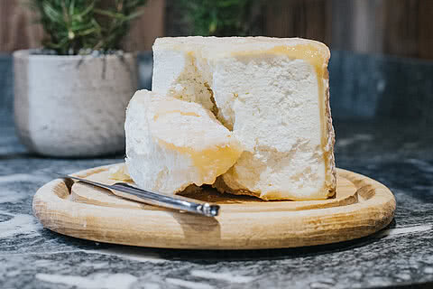 Regionale Käsespezialität auf einem Holzbrett im Hotel Tauernhof Großarl und umgeben von rustikaler Atmosphäre.