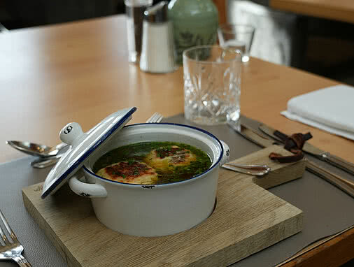 Zwei Kaspressknödel schwimme in einer klaren Suppe in einem kleinen weißen Topf.