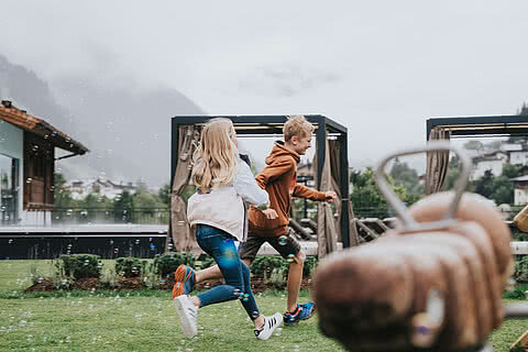 Kinder spielen fröhlich im Garten des Hotels Tauernhof Großarl, umgeben von alpiner Landschaft und moderner Outdoor-Ausstattung.