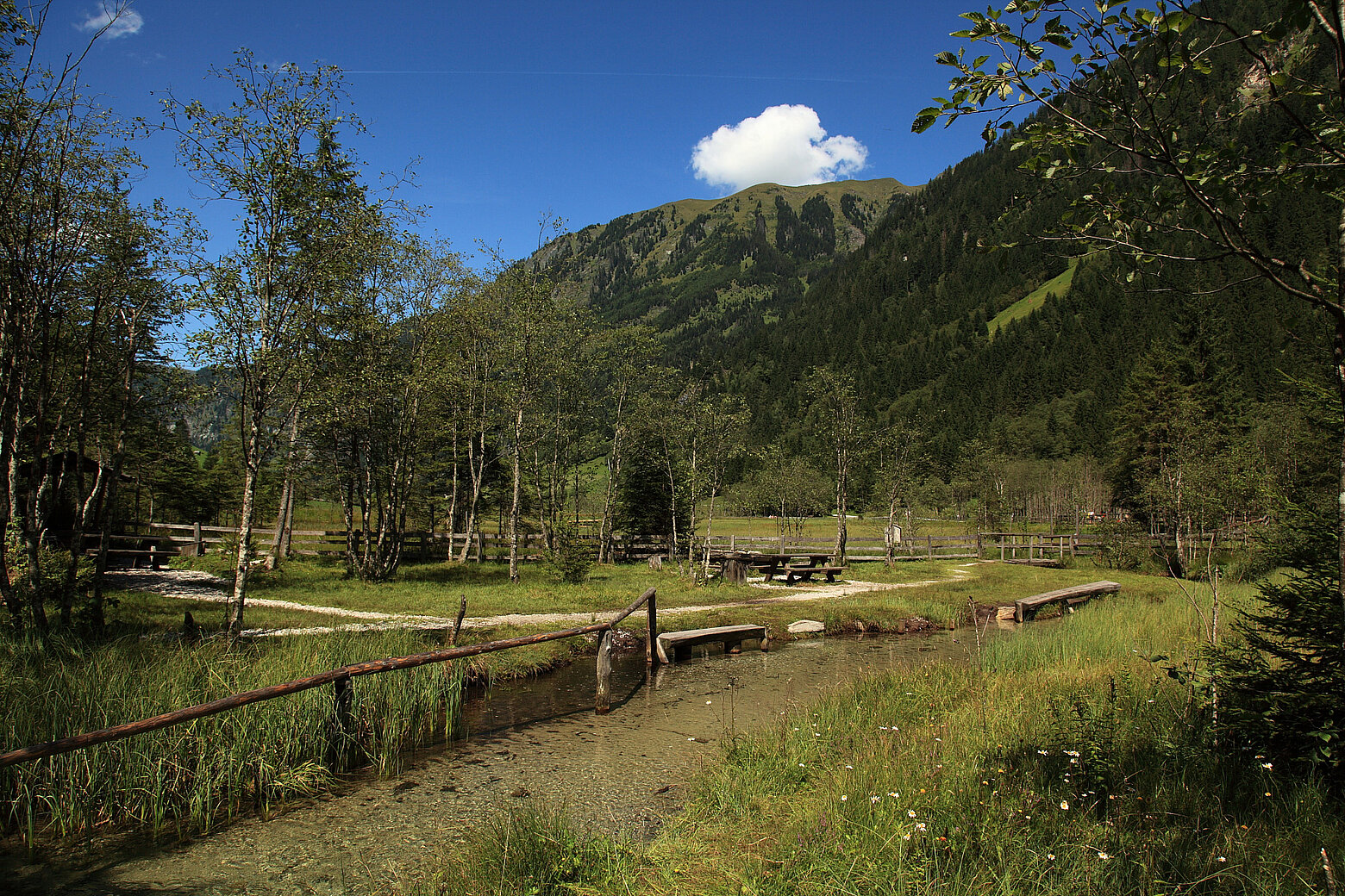 Naturkneippanlage in Hüttschlag nahe dem Hotel Tauernhof Großarl, umgeben von Wiesen, Bäumen und einer alpinen Bergkulisse.