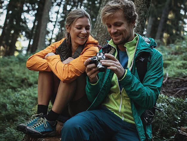 Lächelndes Paar beim Retreat Urlaub betrachtet Fotos auf einer Kamera während einer Wanderung im Wald bei einer Pause