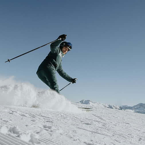 Ein Skifahrer fährt bei strahlendem Sonnenschein und klarem Himmel eine verschneite Piste hinab – perfekte Bedingungen beim Hotel Tauernhof in Großarl.