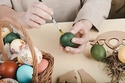 Eine Person bemalt liebevoll ein Osterei, während daneben ein Korb mit bunten Eiern steht. Ostertraditionen werden auch im Hotel Tauernhof in Großarl geschätzt.