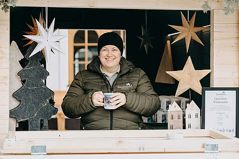 Mitarbeiter des Tauernhof Großarl am Wintermarktstand mit Weihnachtsdekoration und einem heißen Getränk.