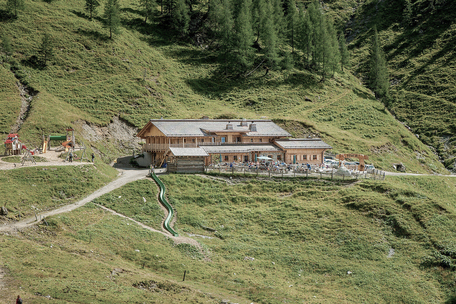 Die Loosbühelalm ist eine große Hütte mit Sonnenterrasse im Großarltal. Hier sieht man sie inmitten grüner Almwiesen im Sommer.