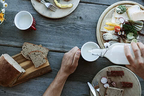 Traditionelles Frühstück mit frischem Bauernbrot, regionalen Aufschnitten, Käse und Milch, serviert auf einem Holztisch nahe dem Hotel Tauernhof Großarl.