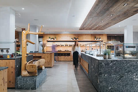 Modernes Buffetrestaurant im Hotel Tauernhof Großarl mit Holz- und Steinelementen, hell beleuchtet und mit vielseitiger Auswahl an Speisen.
